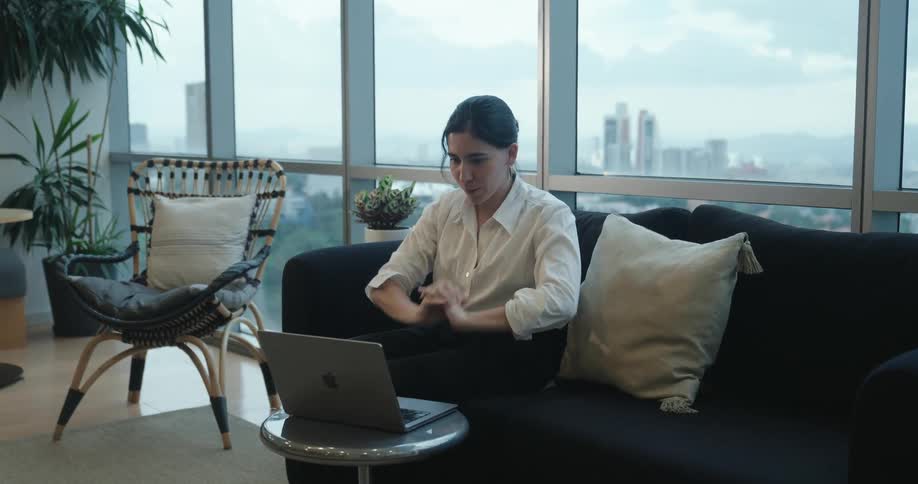 A stressed businesswoman takes a moment to breathe and center herself before continuing to work on her laptop in her modern city apartment