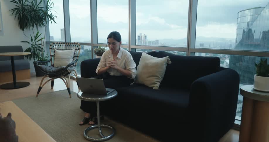 A businesswoman sits down to work on her laptop in a modern office lounge with a scenic city view
