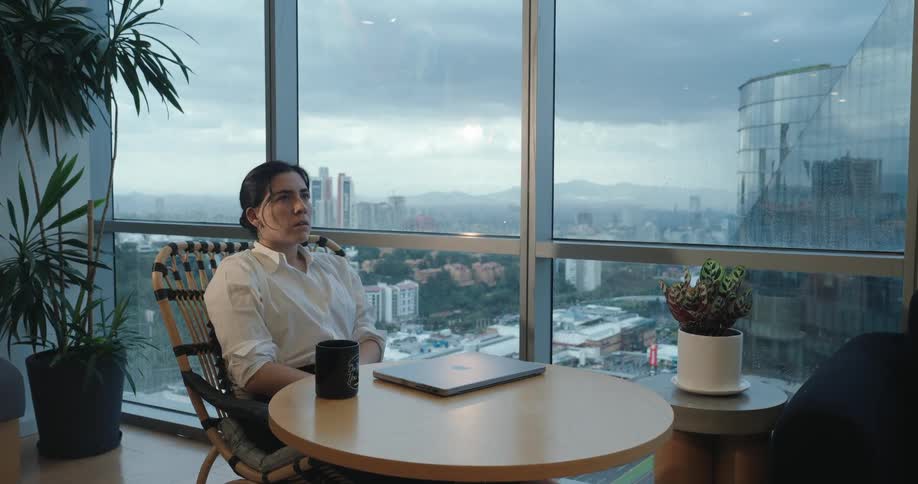 A stressed businesswoman finishes her work on a laptop, closes it, and takes a moment to breathe and de-stress in her modern office overlooking the city