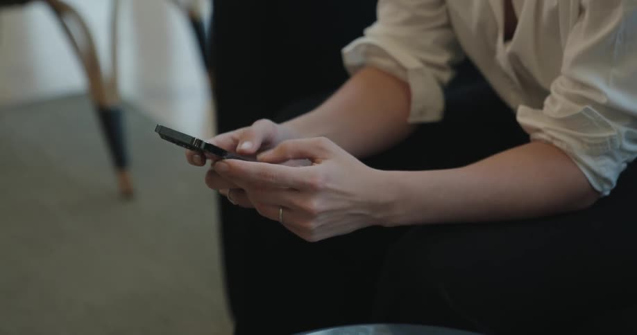 Close-up of a person's hands holding a smartphone while sitting on a couch and scrolling