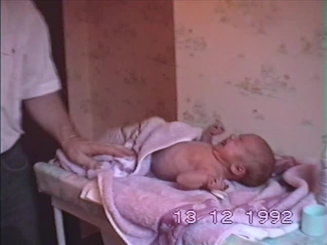 A father dries his crying newborn baby with a pink towel on a changing table in this 1992 home video