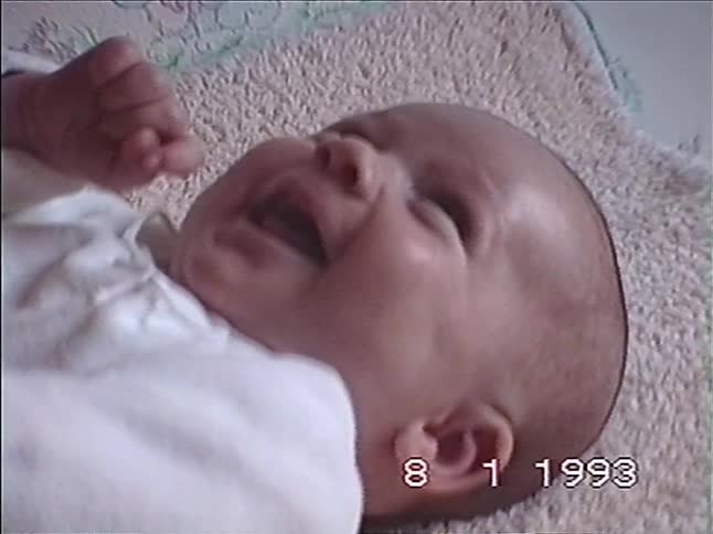 Vintage VHS footage from 1993 shows a close-up of a newborn baby crying while a parent's hand gently touches its face