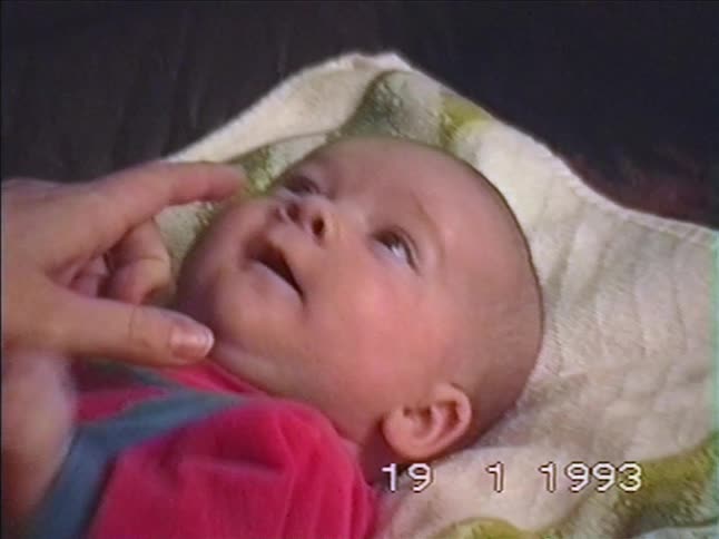 A vintage home video from 1993 showing a parent's hand gently caressing a sleepy newborn baby's face as it yawns