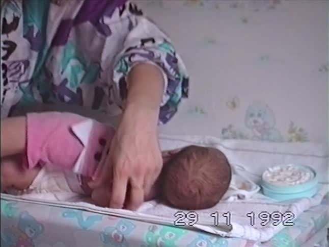 A mother gently washes and dresses her newborn baby on a changing table using a pink puppet washcloth in 1992