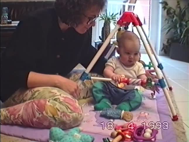 A mother sits with her baby on a playmat as the infant plays with a baby gym in their living room in 1993