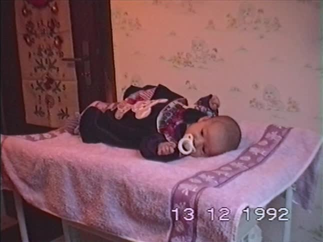 A vintage home video from 1992 shows a calm baby with a pacifier lying on a changing table in a nursery