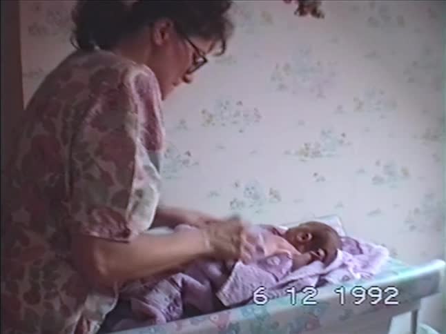 Vintage VHS footage from 1992 shows a loving mother carefully drying and dressing her newborn baby on a changing table