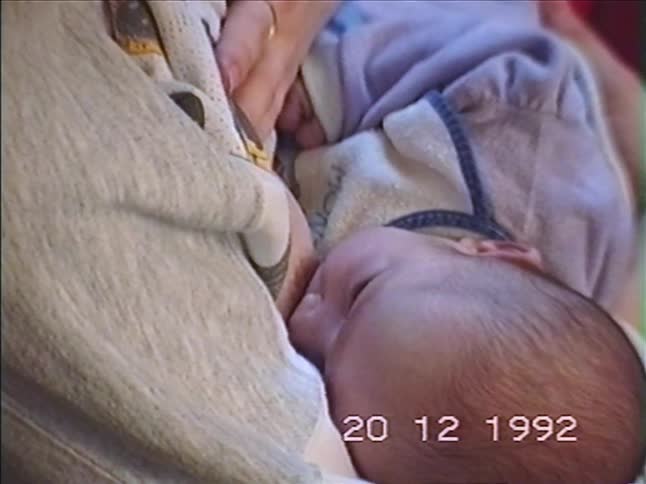 An intimate close-up of a mother breastfeeding her newborn baby, captured on a vintage home video from 1992