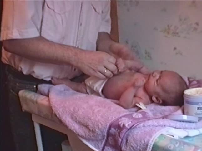 A father gently changes his newborn baby's diaper on a pink changing table in a home setting