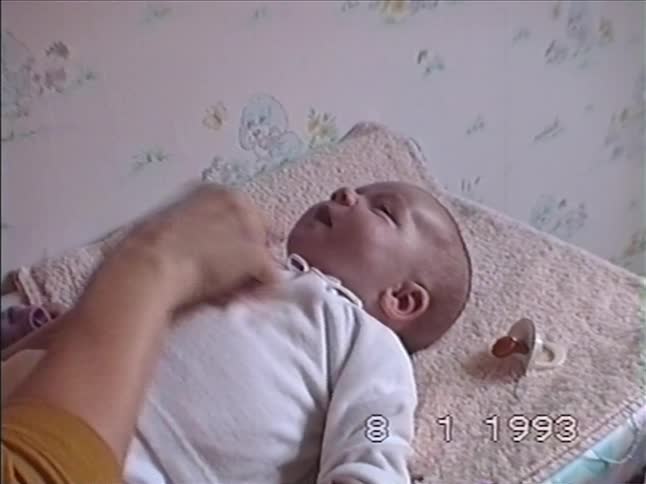 A mother gently cares for her newborn baby, touching its face and chest as it yawns in this vintage 1993 home movie