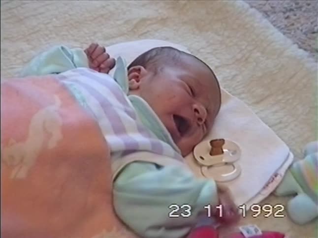 Vintage 1992 footage captures a sleepy newborn baby in pastel pajamas yawning widely as they lie on a soft rug