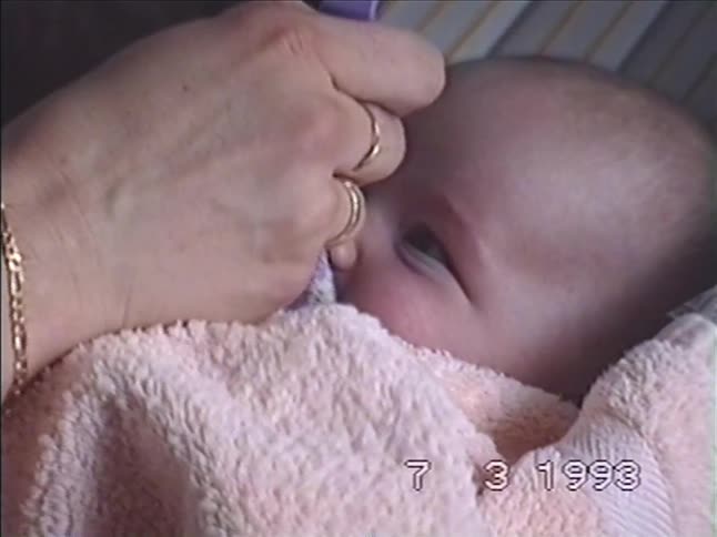 A close-up of a mother feeding her newborn baby with a spoon in a vintage home video from 1993