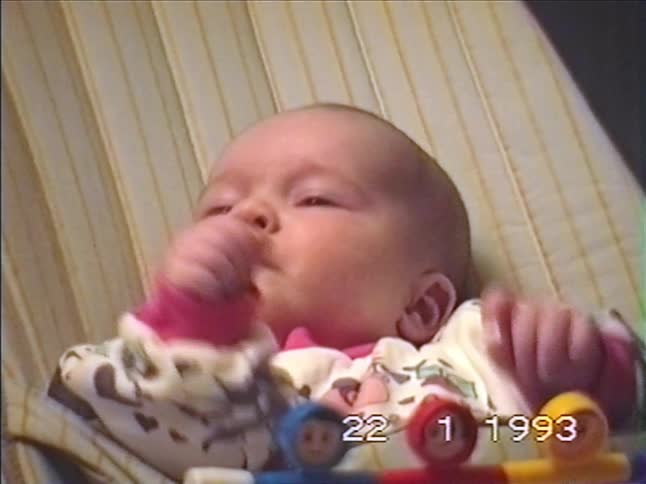 Close-up of a newborn baby in a bouncer making fussy faces, from a 1993 home video