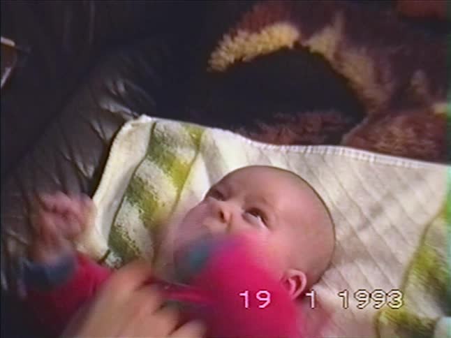 A sweet newborn baby wearing a pink onesie lies on a couch and makes funny faces in a vintage 1993 home video