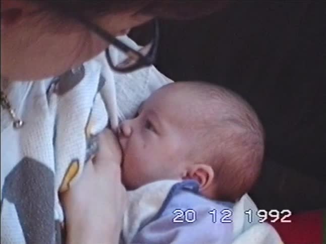 A mother breastfeeds her newborn baby in an intimate close-up from a 1992 home video