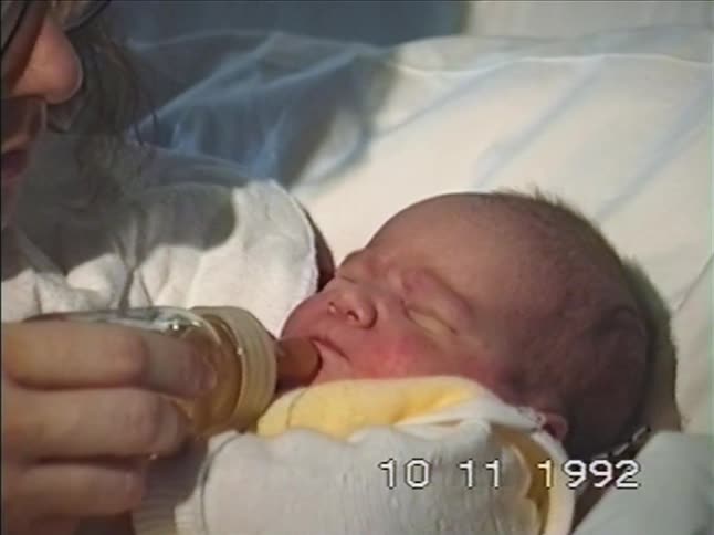 Archival footage from 1992 shows a loving mother gently feeding her newborn baby with a bottle in a hospital bed