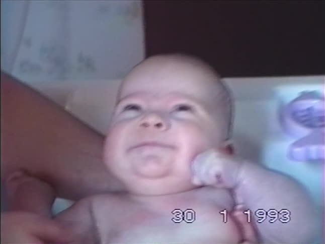 Vintage 1993 VHS footage shows a parent gently bathing their newborn baby, who looks up with a sleepy expression