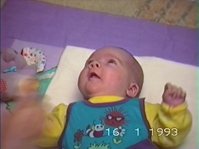 A vintage home video from 1993 shows a mother gently playing with her newborn baby who begins to cry