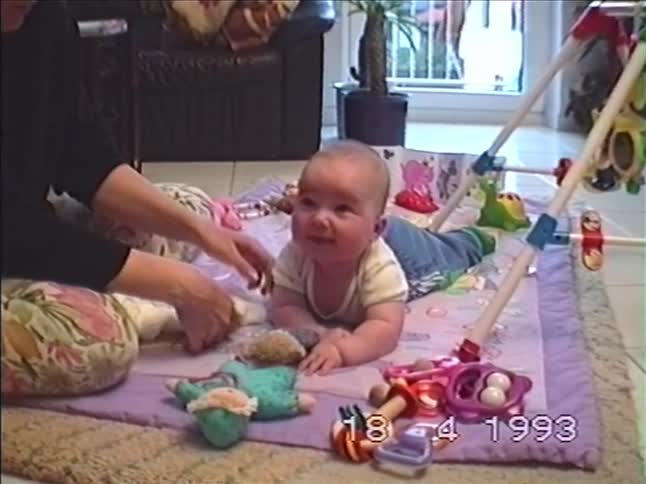 A sleepy baby yawns while lying on a colorful playmat in a nostalgic home video from 1993