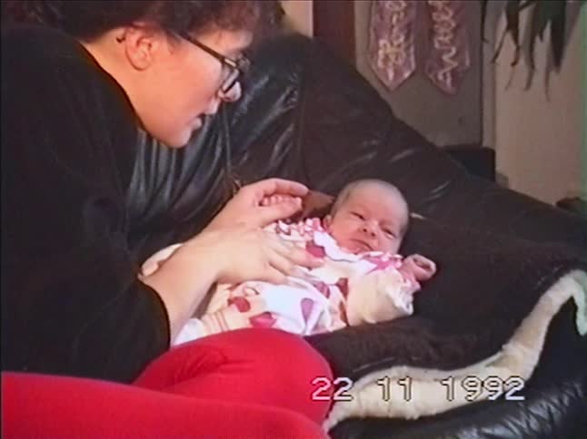 A loving mother gazes at her newborn baby, gently holding its hands as the infant yawns in this vintage 1992 home video
