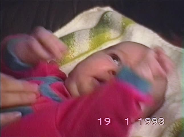 A parent's hand gently caresses their newborn baby's chubby cheek in this heartwarming vintage home video from 1993