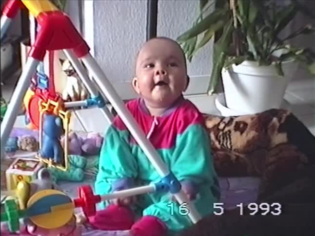 Home video from 1993 shows an adorable baby in a colorful onesie sitting with toys and a baby gym