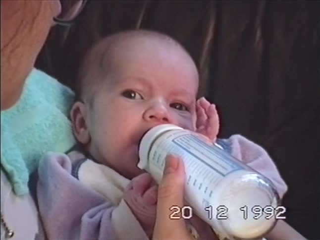 Archival footage from 1992 shows a close-up of a newborn baby being bottle-fed by its mother