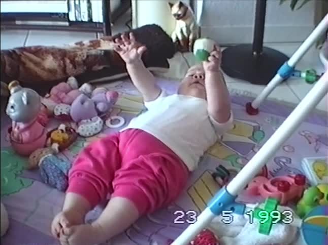 Authentic VHS footage from 1993 shows a cute baby in pink pants lying on a playmat, kicking its feet while playing with a toy ball