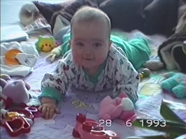 A vintage VHS home video from 1993 shows an adorable baby smiling and kicking their feet while lying on a play mat surrounded by toys