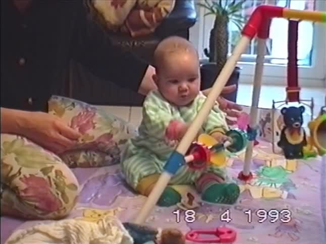 A mother helps her baby play with a colorful baby gym on a playmat at home in 1993