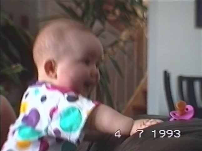 A cute baby in a colorful polka dot shirt laughs and smiles in a home video from 1993