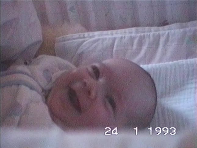 Close-up vintage home movie from 1993 of a sleepy newborn baby yawning and falling asleep in a crib