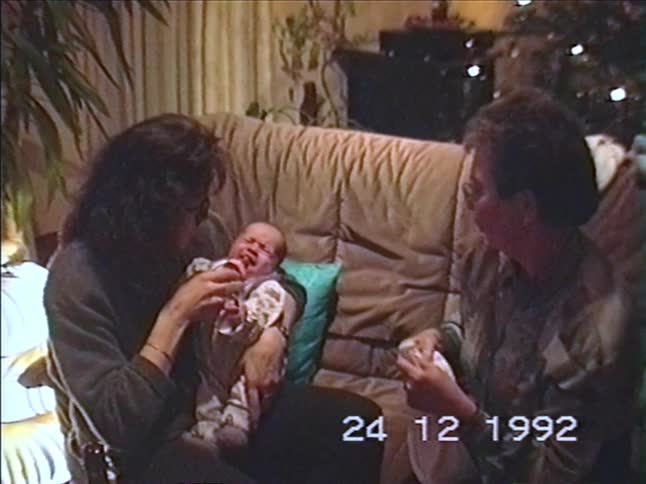 A mother and grandmother comfort a crying newborn with a bottle on Christmas Eve in this authentic 1992 home video