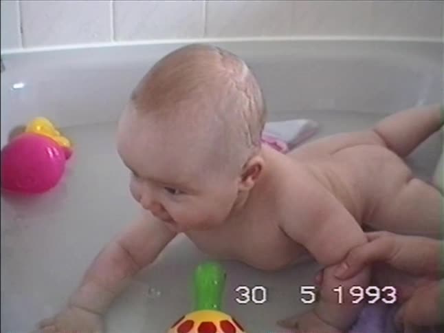 Vintage 1993 VHS footage of a cheerful baby with chubby cheeks smiling during bath time with colorful toys