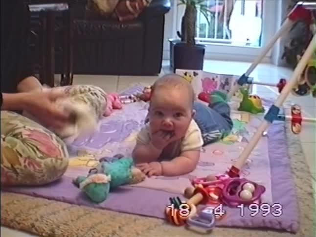 An adorable baby smiles for the camera during playtime on a mat in the living room in 1993