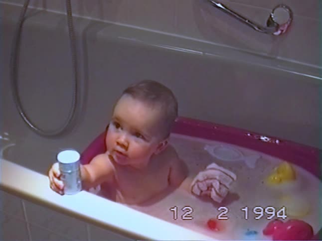 A cute baby smiles happily while playing with toys in a bubble bath in a 1994 home video