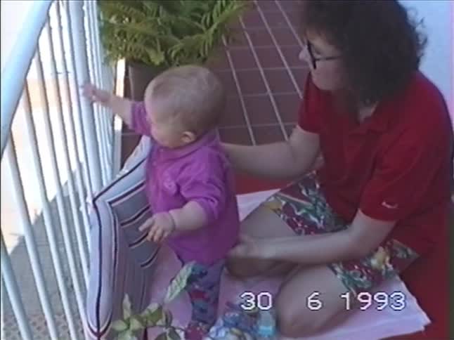 Authentic 1993 home video of a mother helping her baby stand and look out from a sunny tiled balcony