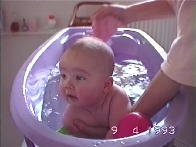 Vintage 1993 VHS footage shows a smiling baby enjoying a bath in a purple tub as their parent washes them