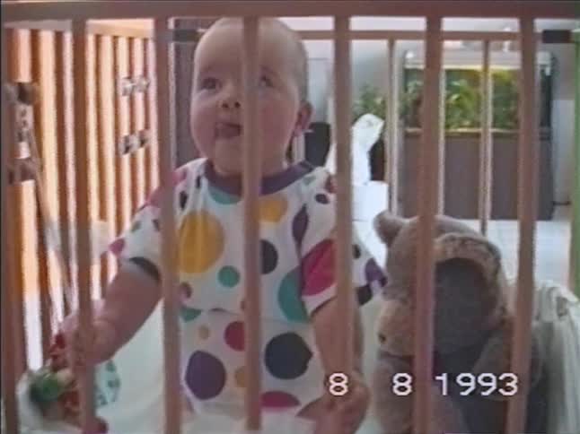 Vintage VHS footage from 1993 shows a happy baby with a big smile standing in a wooden playpen at home