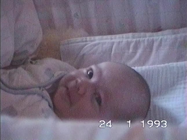 A vintage home movie from 1993 shows an adorable newborn baby smiling and laughing while lying in their crib