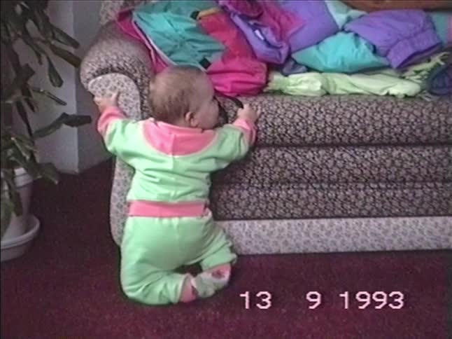Vintage 1993 VHS footage shows an adorable baby in a colorful tracksuit attempting to stand up using the sofa before falling