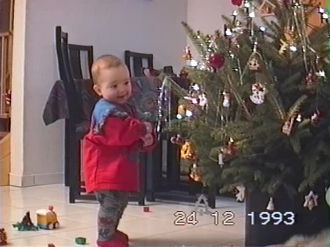 Adorable toddler looks in wonder at a decorated Christmas tree in a vintage home video from 1993