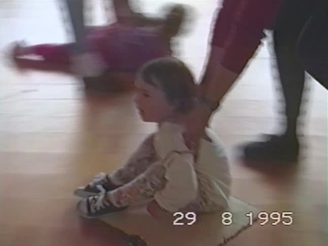 An adult pulls a toddler across a wooden floor on a small mat in this authentic home video from 1995
