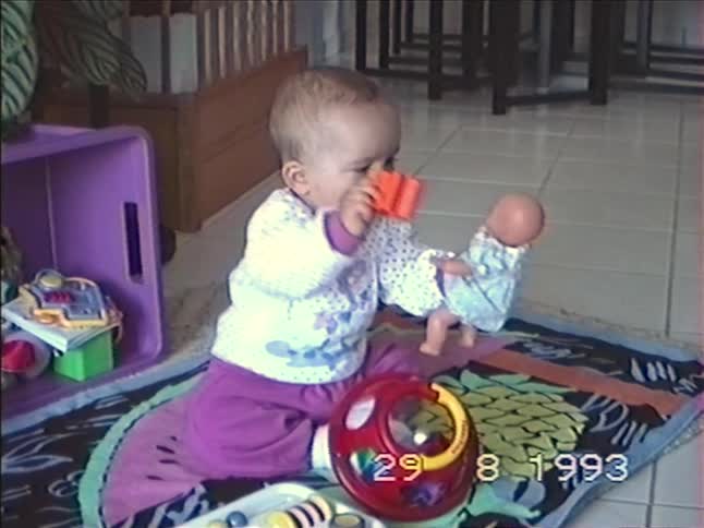 Vintage home movie from 1993 shows a cute baby girl sitting on the floor and playing with her toys and a doll