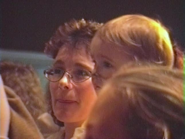 Vintage home video footage shows a mother playfully sticking her tongue out next to her young child with painted whiskers
