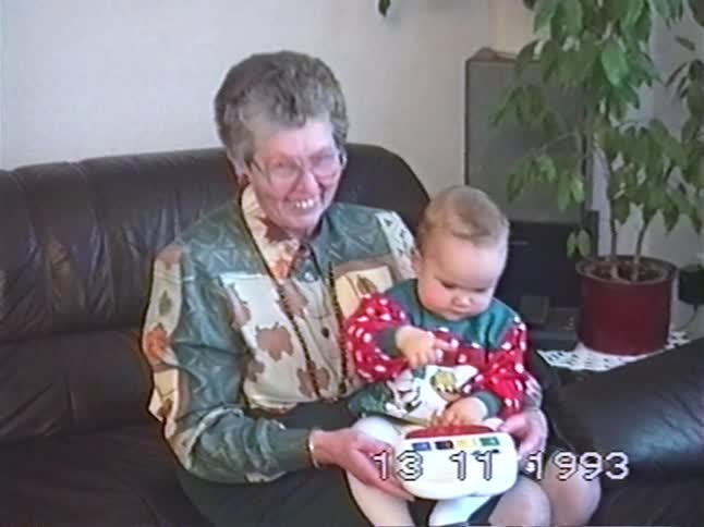 A sweet vintage home video from 1993 shows a grandmother smiling as she holds a baby playing with a toy on her lap