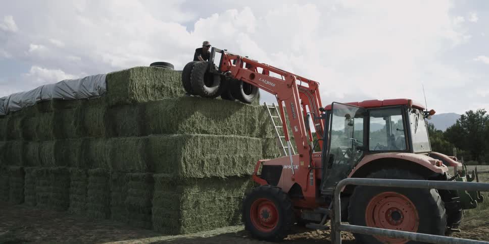 Man standing on top of stacks of hay removing tires from tractor