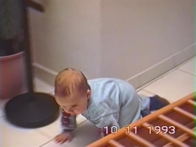 A cute baby in a onesie crawls on the floor after playing with a wooden toy in this vintage 1993 home video