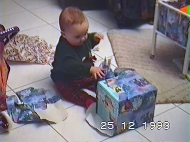 A cute baby excitedly tears the wrapping paper off a large Christmas present in a home video from 1993