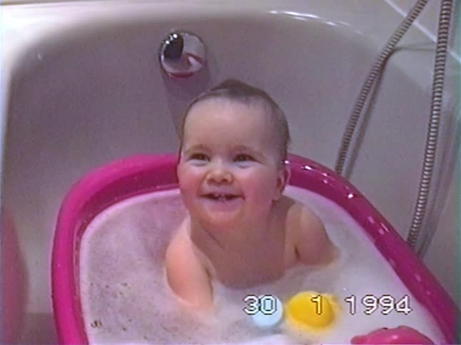 An adorable happy baby laughs and smiles while taking a bubble bath in a vintage home video from 1994